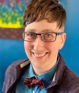 Picture of Danielle, a white person wearing blue collared shirt with purple bowtie, blue glasses and short brown hair
